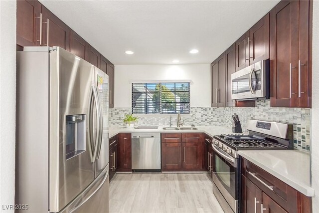 kitchen with stainless steel appliances, a sink, light wood-style flooring, tasteful backsplash, and light countertops