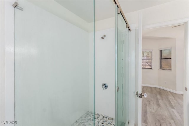 bathroom featuring wood finished floors, a shower stall, and baseboards