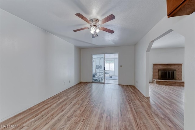 729 Scottsdale St, Henderson, NV 89002 - unfurnished living room with light wood-style flooring, ceiling fan, arched walkways, a fireplace, and a textured ceiling