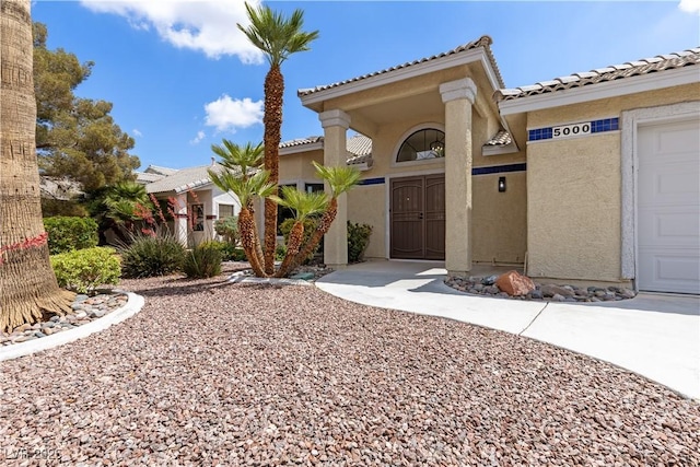 entrance to property with stucco siding, a tile roof, and a garage