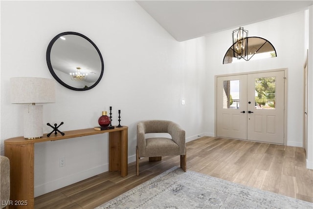 foyer entrance with a chandelier, wood finished floors, vaulted ceiling, baseboards, and french doors