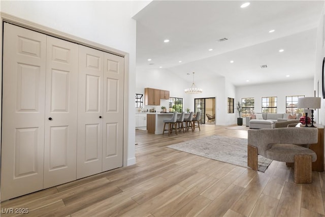 living room with a chandelier, recessed lighting, light wood-type flooring, and high vaulted ceiling