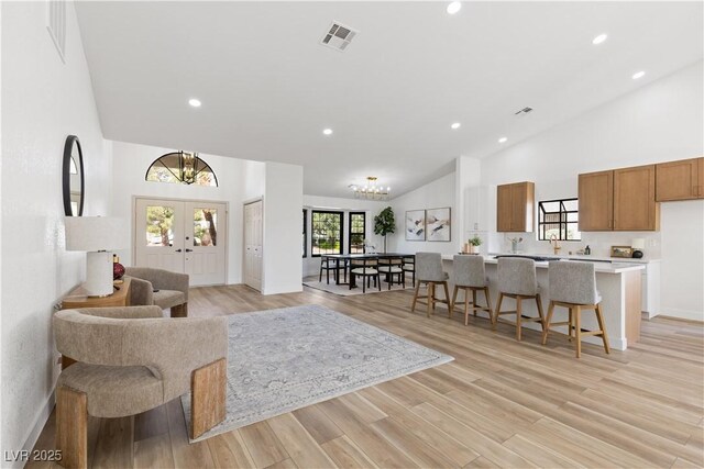 living area with high vaulted ceiling, french doors, recessed lighting, light wood-type flooring, and a chandelier