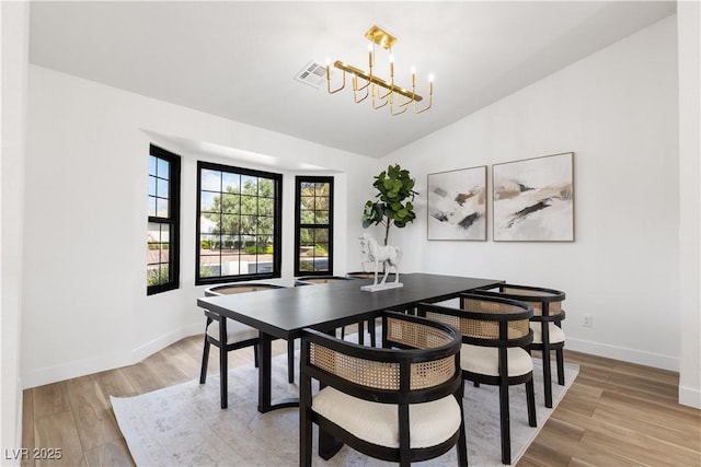 dining area featuring a chandelier, lofted ceiling, light wood-type flooring, and baseboards