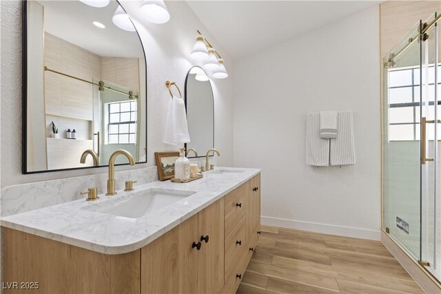 full bath with a stall shower, double vanity, baseboards, and wood finished floors