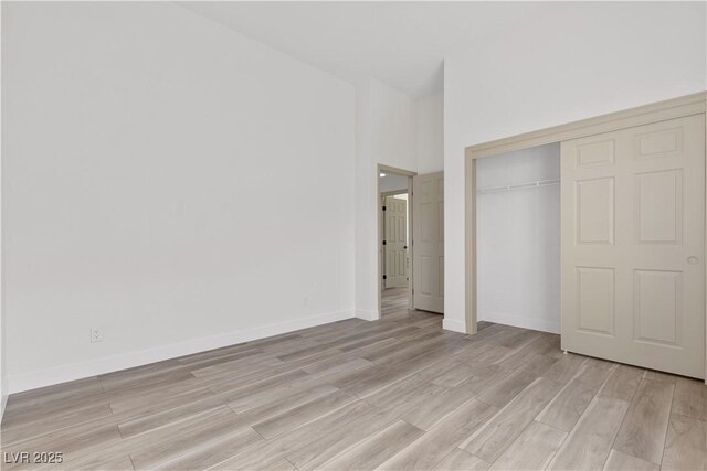 unfurnished bedroom featuring light wood-style flooring, a closet, and baseboards