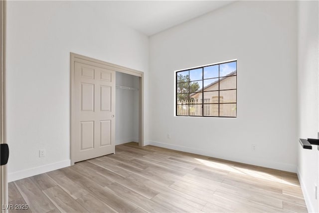 unfurnished bedroom featuring light wood-style floors, baseboards, and a closet