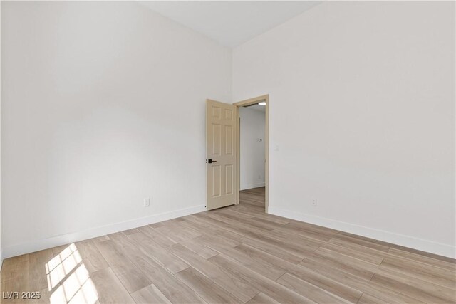unfurnished room with light wood-style floors, baseboards, and a towering ceiling