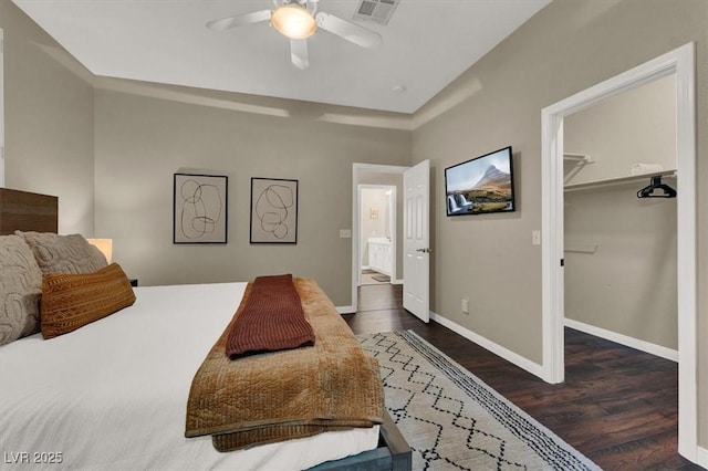 bedroom with wood finished floors, a spacious closet, baseboards, and a ceiling fan