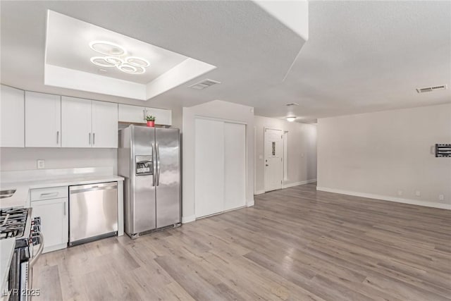 kitchen with appliances with stainless steel finishes, open floor plan, light wood finished floors, light countertops, and white cabinetry