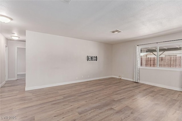 unfurnished room featuring light wood finished floors, baseboards, and a textured ceiling