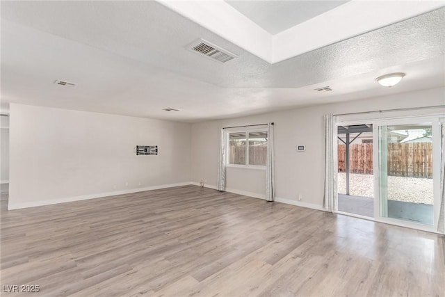 unfurnished room featuring light wood finished floors, healthy amount of natural light, baseboards, and a textured ceiling