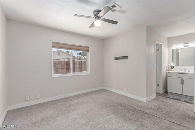 unfurnished bedroom with a sink, light carpet, baseboards, ensuite bathroom, and a ceiling fan