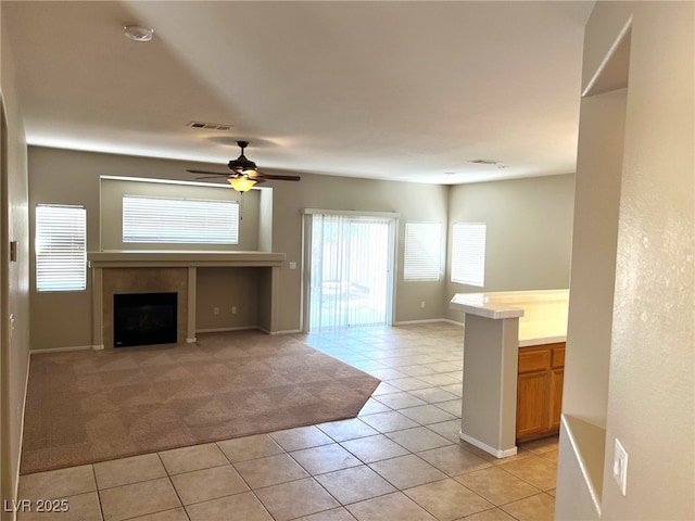 unfurnished living room featuring a tile fireplace, light tile patterned flooring, a ceiling fan, baseboards, and light colored carpet