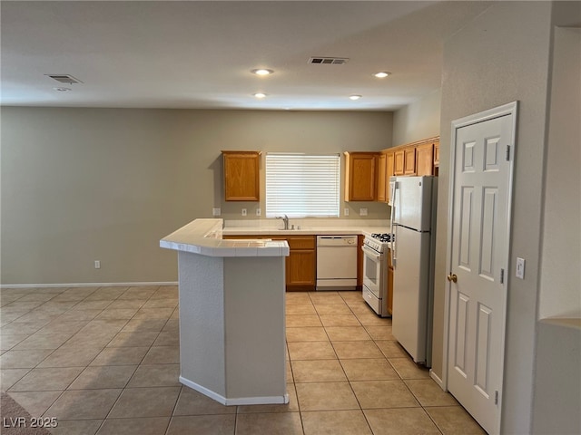 kitchen featuring white appliances, light tile patterned floors, a sink, tile countertops, and a peninsula
