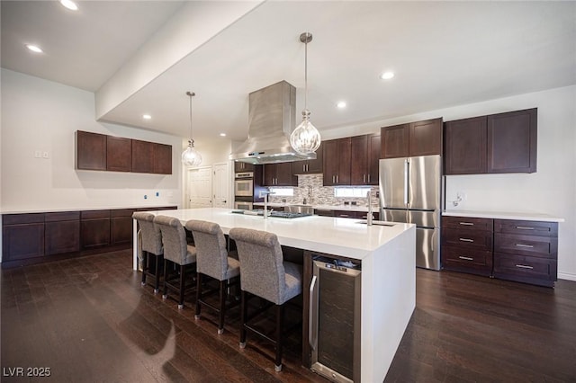 kitchen with freestanding refrigerator, beverage cooler, range hood, dark wood finished floors, and a large island with sink