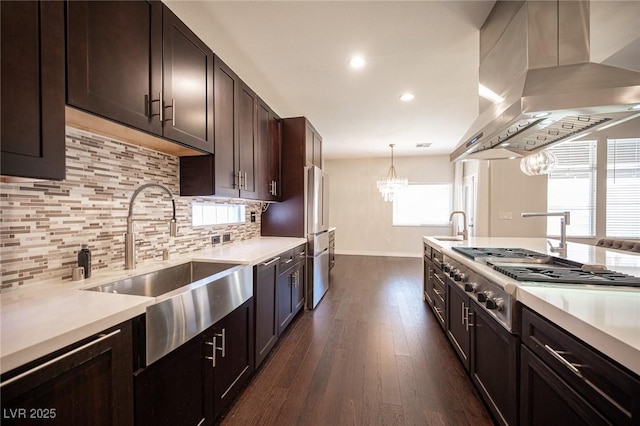 kitchen with wall chimney range hood, a chandelier, baseboards, a sink, and dark wood-style floors