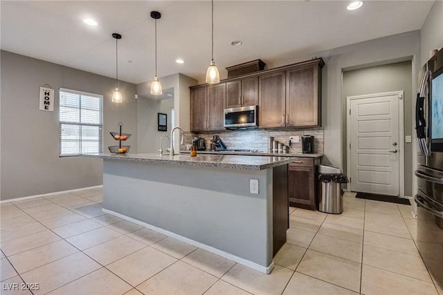 253 Kindly Way, Henderson, NV 89011 - kitchen featuring stainless steel microwave, light tile patterned flooring, backsplash, dark brown cabinetry, and light stone countertops