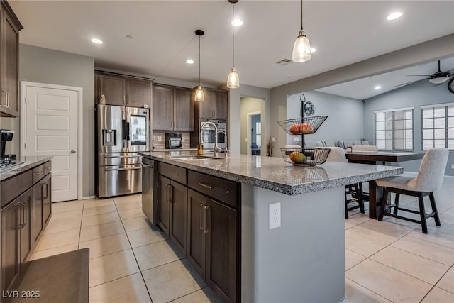 253 Kindly Way, Henderson, NV 89011 - kitchen with appliances with stainless steel finishes, a sink, light tile patterned flooring, dark brown cabinets, and dark stone countertops