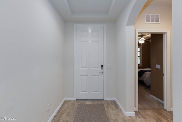 doorway featuring arched walkways, light wood-style flooring, and baseboards