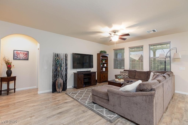 living area with arched walkways, a ceiling fan, light wood-type flooring, and baseboards