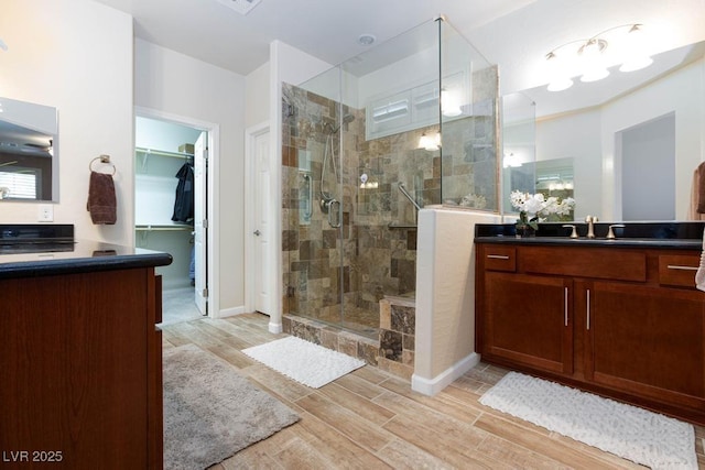 bathroom featuring a stall shower, wood tiled floors, a spacious closet, vanity, and baseboards