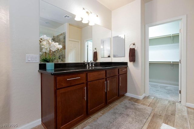 full bathroom featuring wood finished floors, a walk in closet, vanity, and baseboards