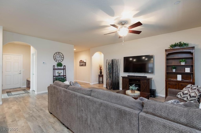 living area with arched walkways, a ceiling fan, light wood-type flooring, and baseboards
