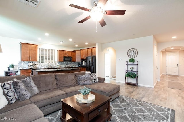 living room featuring arched walkways, ceiling fan, light wood-style floors, recessed lighting, and baseboards