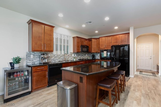 kitchen featuring black appliances, beverage cooler, a sink, arched walkways, and tasteful backsplash