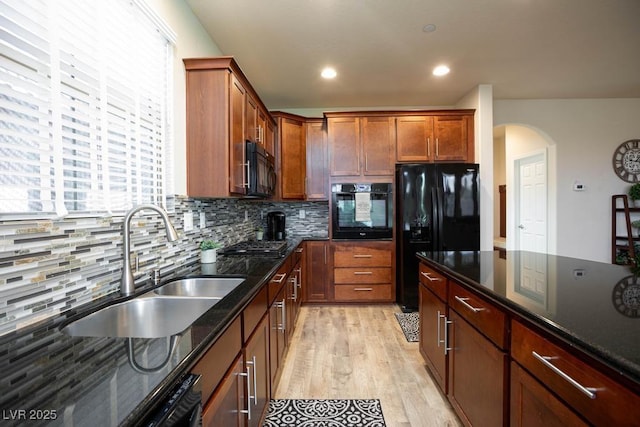 kitchen with black appliances, a sink, light wood finished floors, backsplash, and arched walkways