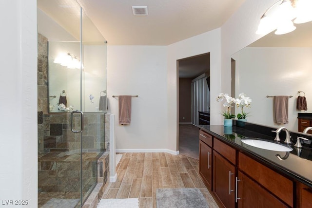 full bathroom with a shower stall, vanity, wood finish floors, and baseboards