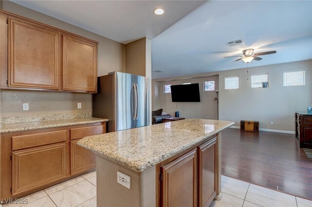 3440 Bella Viera Ct, Las Vegas, NV 89141 - kitchen featuring freestanding refrigerator, ceiling fan, a kitchen island, light stone countertops, and brown cabinetry