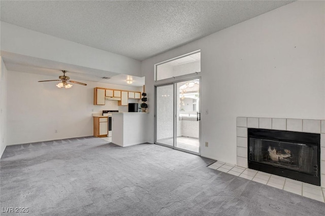 unfurnished living room featuring light colored carpet, a tiled fireplace, ceiling fan, and a textured ceiling