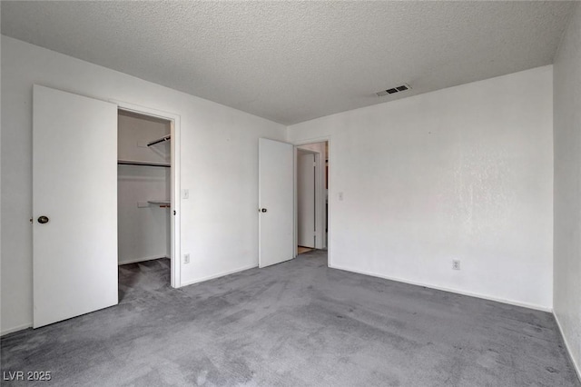 unfurnished bedroom featuring carpet floors, a textured ceiling, a spacious closet, baseboards, and a closet