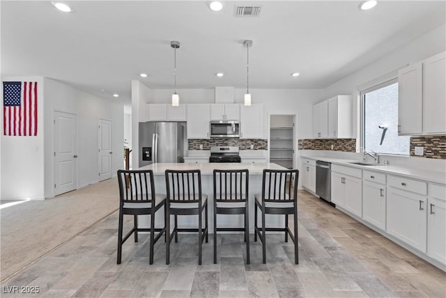 kitchen with appliances with stainless steel finishes, a sink, a breakfast bar area, white cabinets, and decorative backsplash