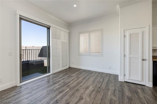 empty room with wood finished floors, plenty of natural light, crown molding, and baseboards