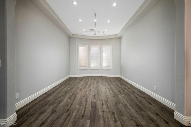 spare room featuring dark wood-type flooring, recessed lighting, baseboards, and a raised ceiling