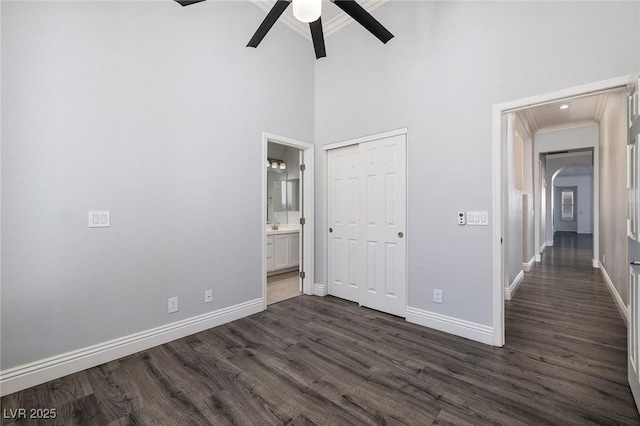 unfurnished bedroom featuring a towering ceiling, baseboards, dark wood-style flooring, crown molding, and a closet