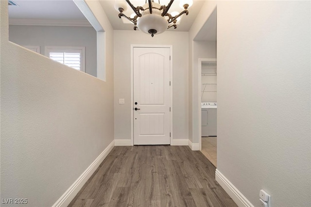 entrance foyer featuring washer / clothes dryer, a chandelier, dark wood finished floors, baseboards, and ornamental molding