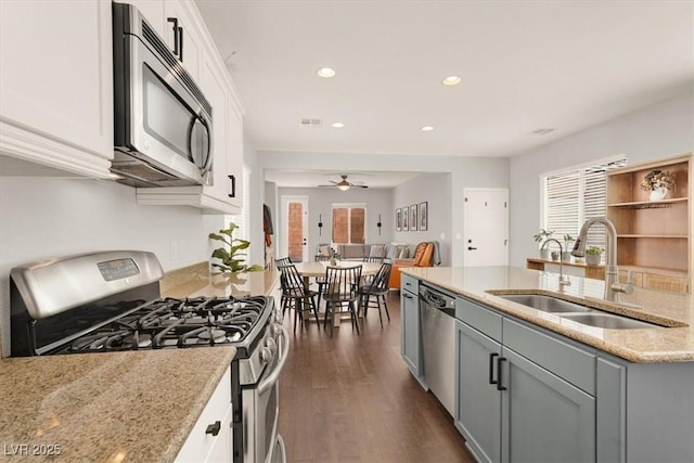 kitchen with appliances with stainless steel finishes, a sink, light stone countertops, recessed lighting, and dark wood-style floors