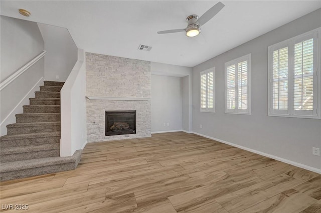 unfurnished living room with healthy amount of natural light, a ceiling fan, wood finished floors, and stairway