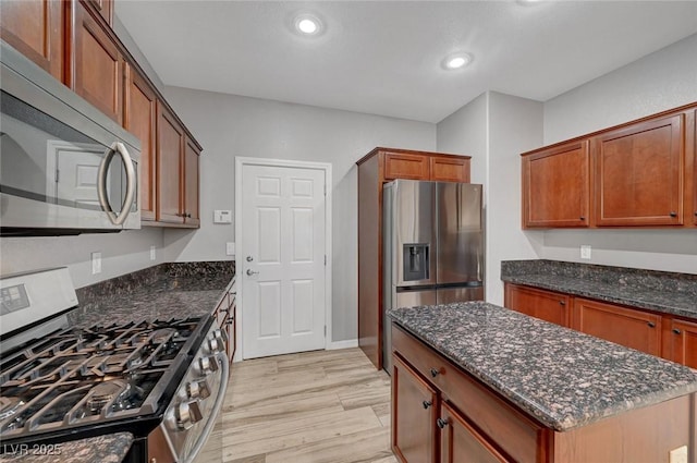kitchen with stainless steel appliances, dark stone counters, light wood-style flooring, a center island, and recessed lighting