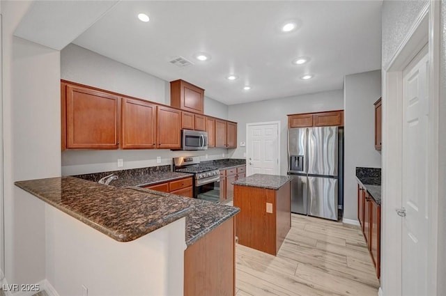 kitchen featuring appliances with stainless steel finishes, a kitchen island, brown cabinets, dark stone countertops, and recessed lighting