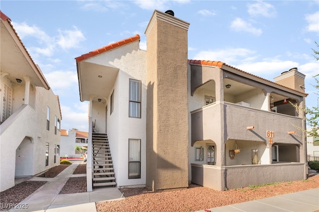 611 Bass Dr Unit C, Henderson, NV 89014 - view of side of property featuring a chimney, stucco siding, stairs, a tile roof, and a balcony