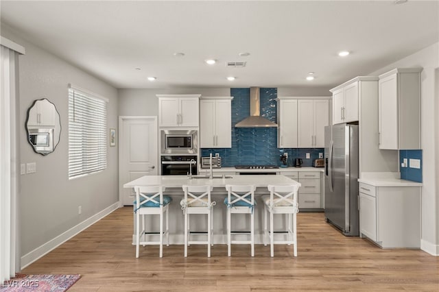 5449 Hickory Tree St, Las Vegas, NV 89149 - kitchen featuring appliances with stainless steel finishes, wall chimney exhaust hood, a breakfast bar area, light countertops, and an island with sink