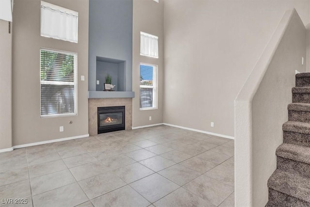 unfurnished living room with stairs, a high ceiling, baseboards, tile patterned flooring, and a tiled fireplace