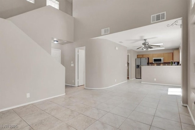 unfurnished living room with ceiling fan, light tile patterned floors, baseboards, a sink, and a high ceiling