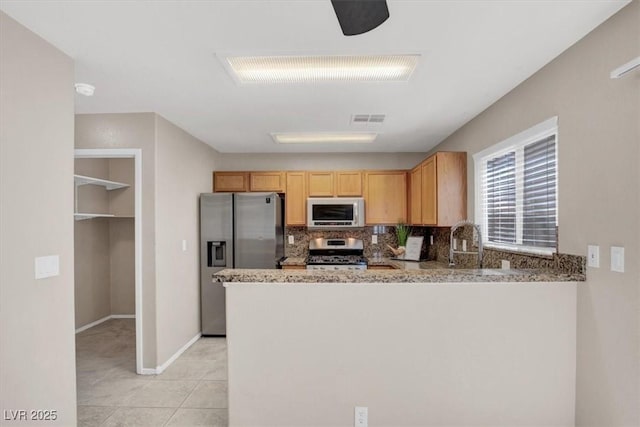 kitchen with appliances with stainless steel finishes, light stone countertops, backsplash, a peninsula, and baseboards
