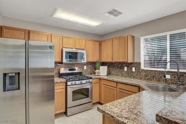 kitchen featuring appliances with stainless steel finishes, a sink, tasteful backsplash, and light stone counters